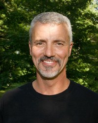 Smiling man outdoors with green trees background.