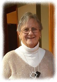Smiling elderly woman with glasses and white sweater.