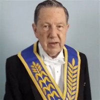 Elderly man in ceremonial attire with sash.