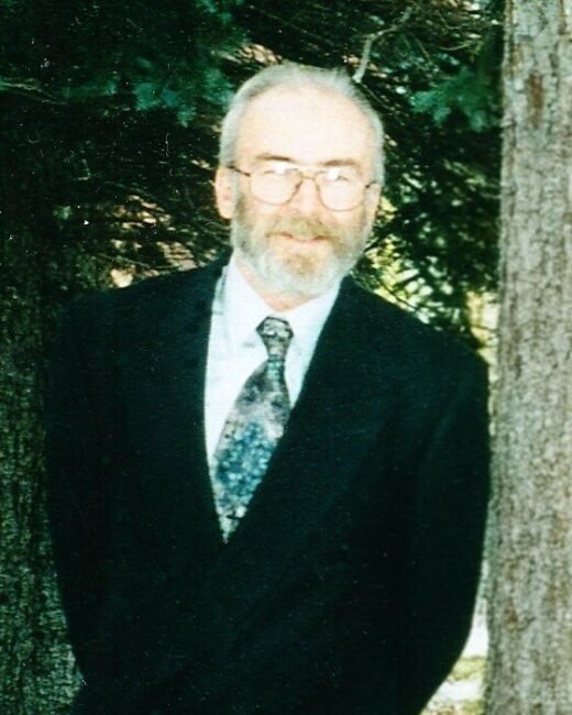 Man in suit standing outdoors near trees.