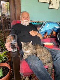 Man relaxing with cat on his lap, holding drink.