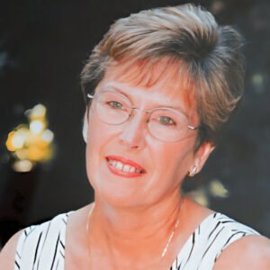 Woman smiling in glasses, striped top, outdoor setting.