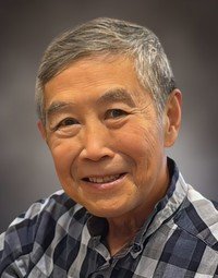Smiling person wearing a checkered shirt against gray background.