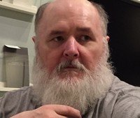 Bearded man sitting indoors, looking to the side.
