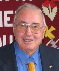 Smiling elderly man with glasses and blue shirt.