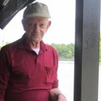 Elderly man in red shirt by riverside