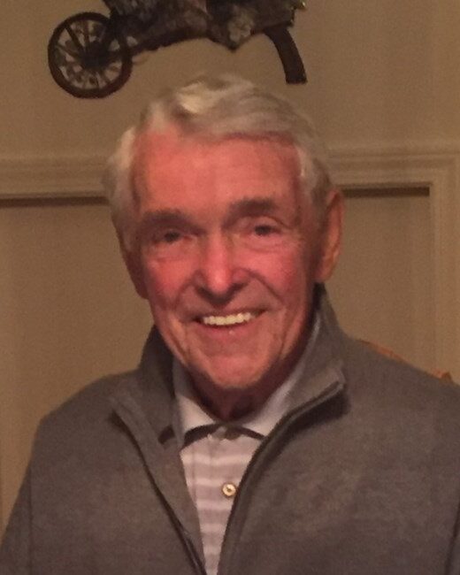 Smiling elderly man in a gray jacket indoors.