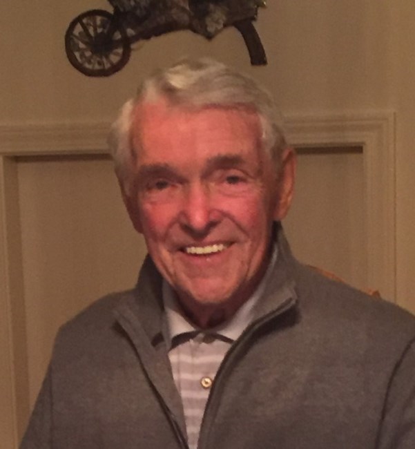 Smiling elderly man in a gray jacket indoors.