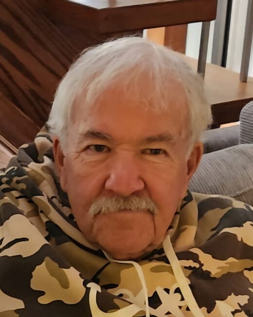 Older man in camouflage hoodie seated indoors