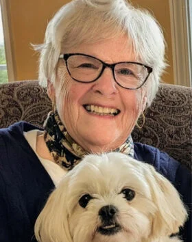 Smiling woman with glasses and small white dog.
