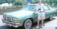 Person standing beside vintage green car on bridge.