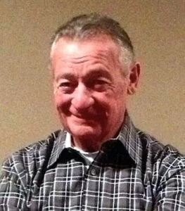 Smiling man in plaid shirt against plain background.