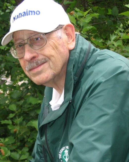 Elderly man in green jacket and cap outdoors.