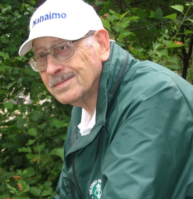 Elderly man in green jacket and cap outdoors.
