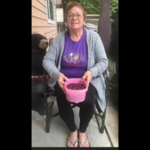 Woman sitting with pink bucket of berries.