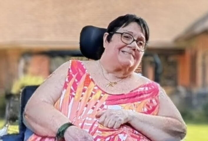 Smiling person in colorful dress using wheelchair outdoors.