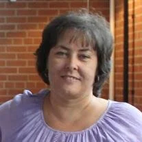 Person smiling, standing indoors near brick wall.
