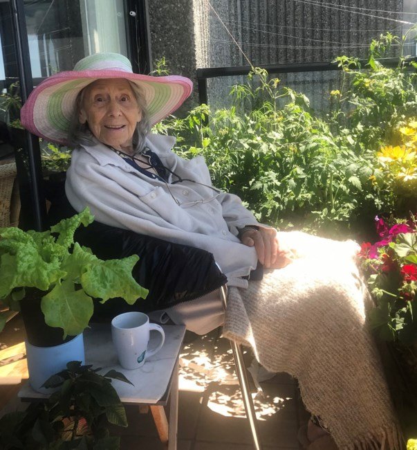 Elderly woman relaxing on balcony with plants.