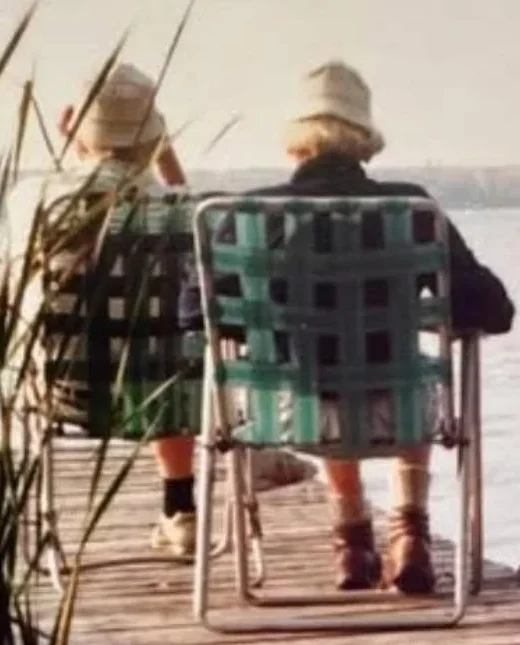 Two people sitting on a lake dock.