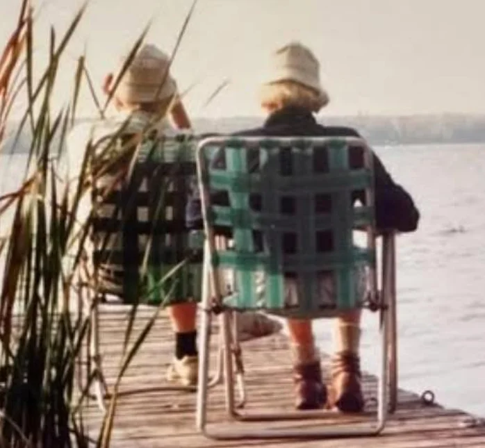 Two people sitting on a lake dock.