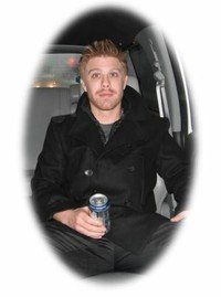 Man in coat sitting with a drink in hand.