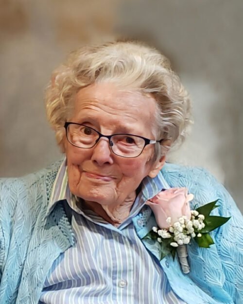 Elderly woman in glasses with pink rose corsage.