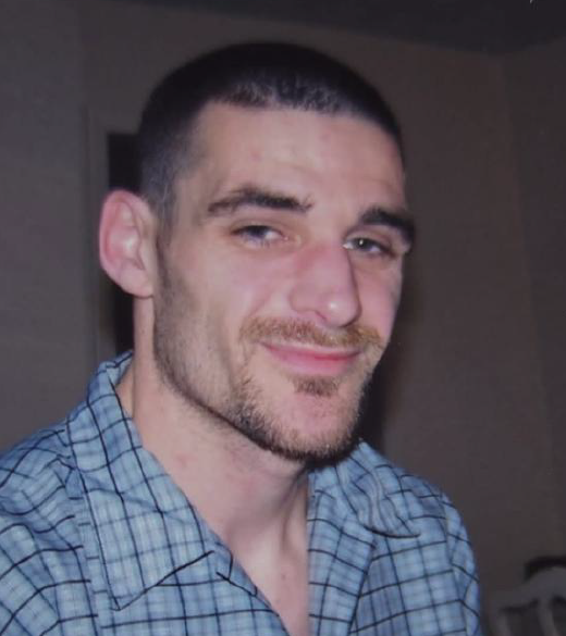 Smiling man in blue checkered shirt indoors.