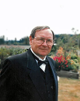 Man in formal attire outdoors with flowers.