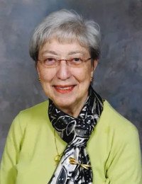 Elderly woman smiling, wearing glasses and scarf.