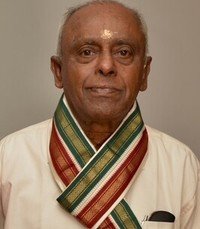 Elderly man wearing traditional attire and a colorful shawl.