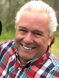 Smiling man in colorful plaid shirt outdoors.