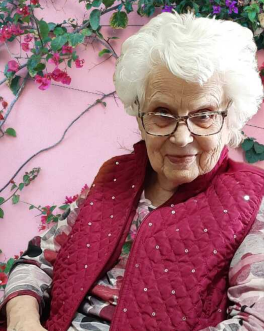 Elderly woman smiling against pink floral background.