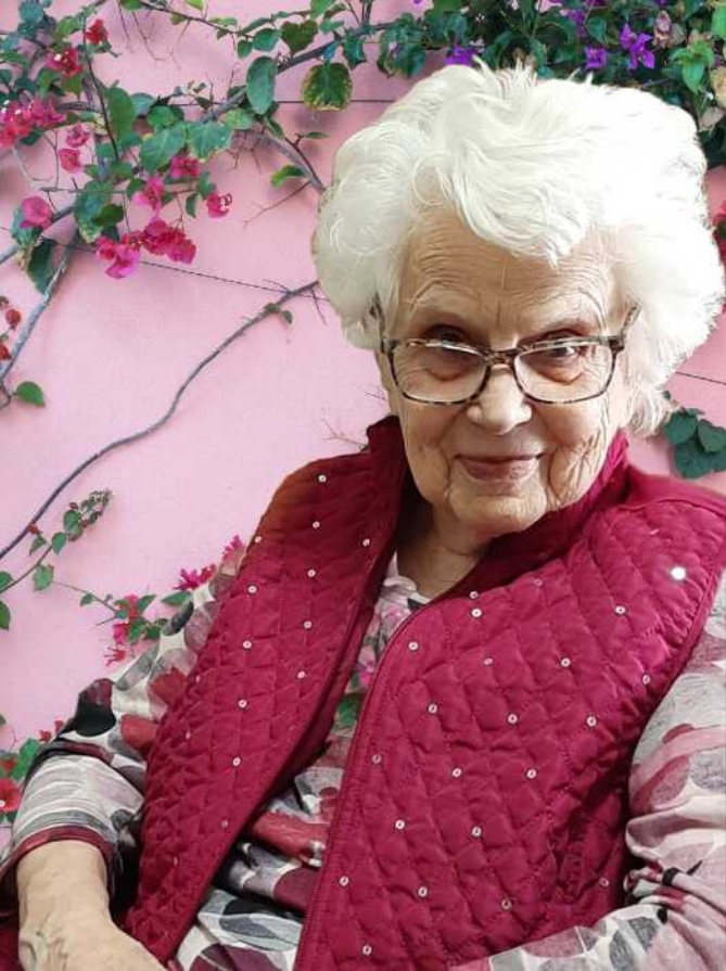 Elderly woman smiling against pink floral background.