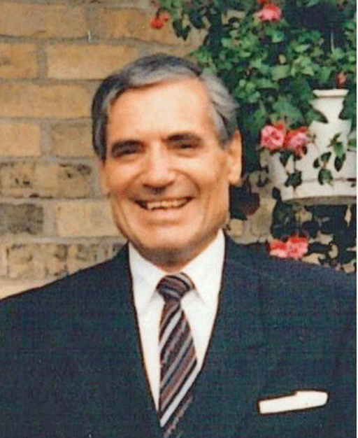 Smiling man in suit with brick background.