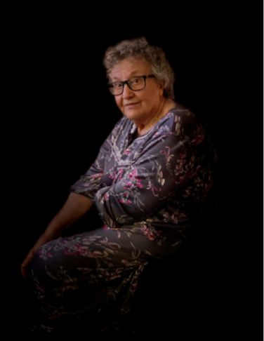 Elderly woman sitting, wearing floral dress, glasses