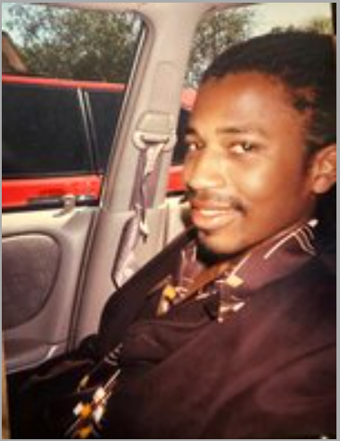 Man smiling in car wearing patterned shirt.