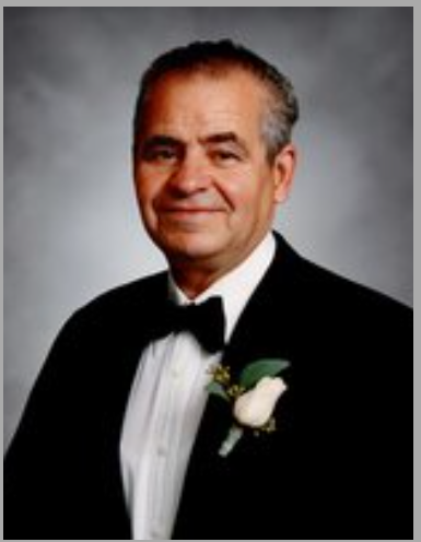 Man in tuxedo with boutonnière, smiling.