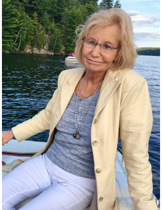Woman seated on boat near forested lake.