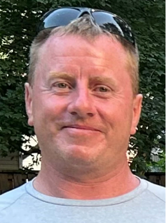 Smiling person outdoors wearing a gray shirt and sunglasses.
