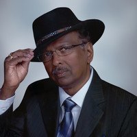 Man in suit and hat, adjusting glasses.