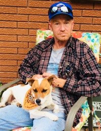 Man sitting outdoors with small dog on lap.