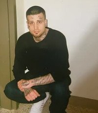 Person crouching in a black sweater and tattoos.