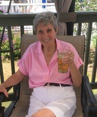 Elderly woman sitting outdoors with iced drink.