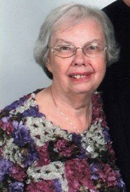 Smiling elderly woman with glasses and floral top.