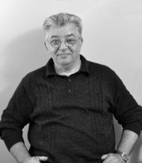 Man smiling with glasses, wearing a black sweater.