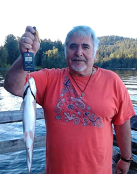 Man holding fish by lakeside with trees behind.