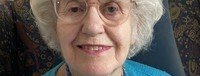 Elderly woman smiling with glasses and white hair.