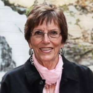 Smiling woman wearing glasses and a scarf outdoors.