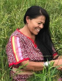Woman smiling in grassy field, wearing floral dress.