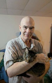 Man smiling while holding a cat indoors.